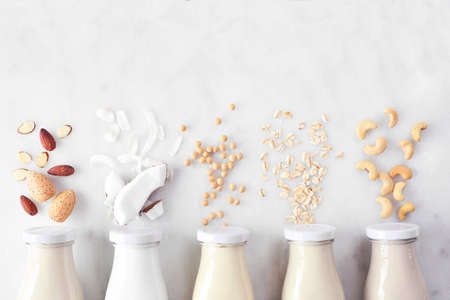 Vegan, plant based, non dairy milk. Variety in milk bottles with ingredients. Above view over a white marble background.の写真素材