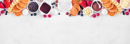 Breakfast or brunch pancake buffet top border. Overhead view on a white marble banner background....
