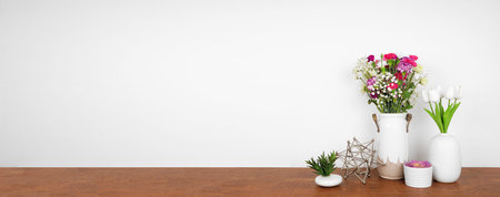Home decor on a wood shelf. Succulent plants and vases of flowers against a white wall. Banner with...