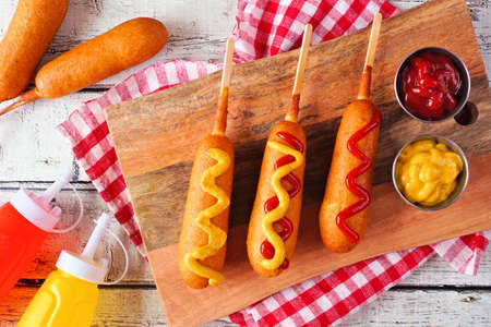 Corn dogs with mustard and ketchup. Top view table scene over a white wood background.の写真素材