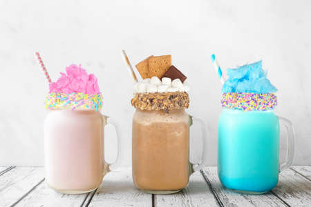 Fun colorful summer milkshakes in mason jar glasses against a white background. Blue and pink cotton candy and chocolate smores sweet drinks.の写真素材