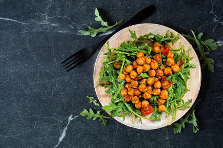 Salad of arugula and seasoned chickpeas. Top down view on a wooden plate over a dark background.の写真素材