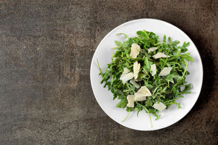Simple salad of arugula and parmesan cheese. Overhead view on a white plate over a dark background.の写真素材