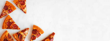 Pepperoni pizza slice corner border. Above view over a white marble banner background. Copy space.の写真素材