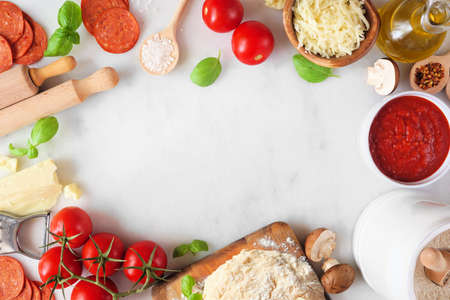 Pizza making ingredients including cheese, pepperoni, tomatoes and basil. Top down view frame against a white marble background. Copy space.の写真素材