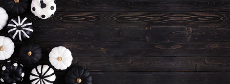 Halloween corner border of black and white patterned pumpkins. Top down view on a black wood banner background. Copy space.の写真素材