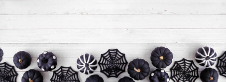 Halloween bottom border of black and white patterned pumpkins and spider web decor. Top down view on a white wood banner background. Copy space.の写真素材