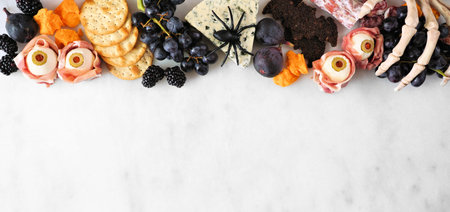 Halloween theme charcuterie top border against a white marble background. Collection of cheeses and...