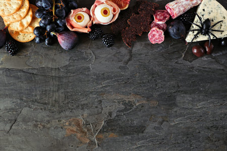 Halloween theme charcuterie top border against a dark stone background. Selection of cheeses and...