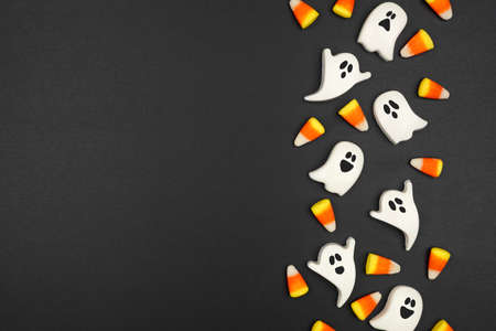 Halloween side border of candy corn and spooky chocolate ghosts. Overhead view on a black background. Copy space.の写真素材