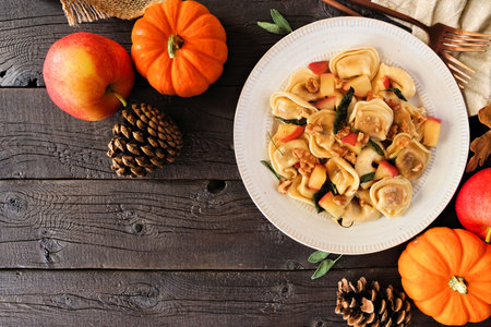Fall pumpkin and apple tortellini pasta with walnuts and brown butter sage sauce. Overhead view table scene on a dark wood background. Copy space.の写真素材