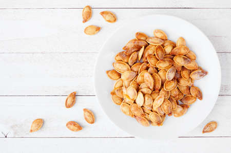 Plate of fall pumpkins seeds, salted and roasted. Top view over a white wood background. Halloween treat.の写真素材
