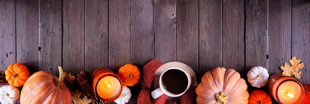 Cozy fall bottom border with pumpkins, sweaters, candles and coffee. Top view over a dark wood...