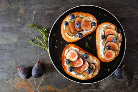 Crostini appetizers with figs, cream cheese spread and blueberries. Overhead view on a dark slate background.の写真素材