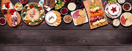 Christmas charcuterie top border against a dark wood banner background. Variety of cheese and meat appetizers. Christmas tree, wreath and candy cane arrangements. Copy space.の写真素材