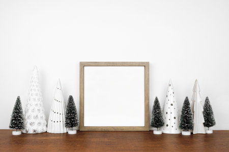 Christmas mock up with wooden frame and tree decor. Square frame on a white shelf against a white wall. Copy space.の写真素材