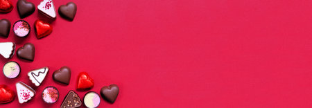 Valentines Day chocolate corner border. Red and pink heart theme. Top view on a red paper banner background with copy space.の写真素材