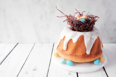 Easter bundt cake with chocolate nest of colorful candy eggs. Side view against a bright wood...