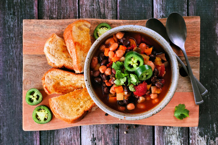 Homemade vegetarian chili with garlic bread on a wooden serving board. Top view table scene on a dark wood background.の写真素材