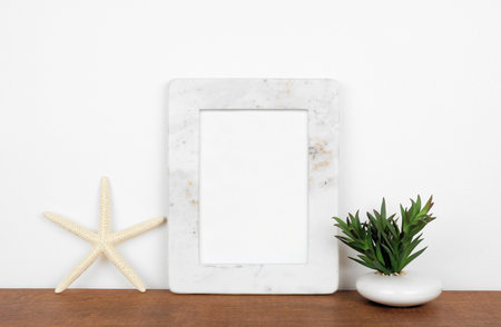 Mock up white marble frame with starfish and succulent plant on a shelf or desk. Wood shelf and white wall. Portrait frame orientation.の写真素材