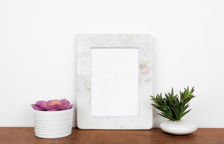 Mock up white marble frame with succulent plants on a shelf or desk. Wood shelf and white wall. Portrait frame orientation.の写真素材