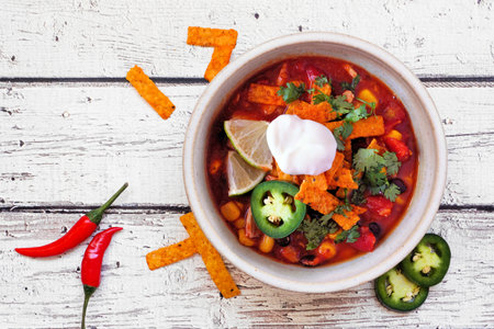 Chicken tortilla soup with tomatoes and black beans. Mexican food dish. Top down view on a white wood background.の写真素材
