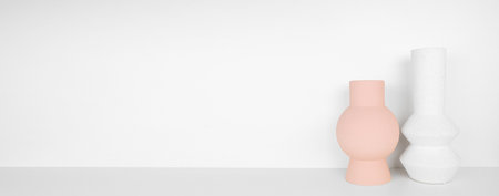 Modern pink and white home decor on a shelf. Geometric vases on a white shelf against a white wall background. Banner with copy space.の写真素材