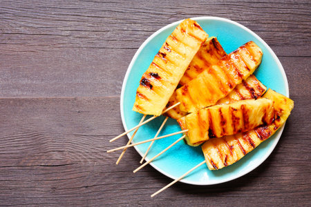 Sweet grilled summer pineapple wedges. Top view over a dark wood background.の写真素材
