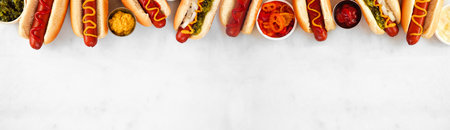Group of hot dogs with an assortment of toppings and condiments. Above view top border on a white marble background.の写真素材