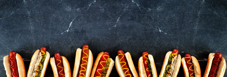 Assortment of hot dogs with a variety of toppings. Top view bottom border on a dark stone background.の写真素材