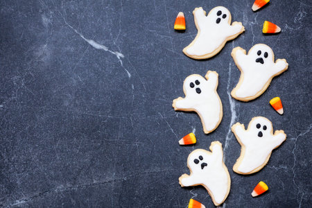 Halloween ghost cookie side border. Top down view on a dark stone background with copy space.