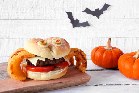 Halloween spider hamburger with onion ring legs. Side view close up  against a white wood background.の写真素材