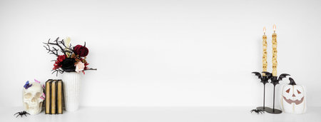 Elegant Halloween or gothic shelf decor with copy space against a white wall banner background. White shelf with skull and butterflies, red and black flowers, jack o lantern, books and candles.の写真素材