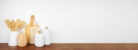 Autumn theme kitchenware, utensils and decor on a wood shelf or counter. Banner against a white wall background with copy space. Fall kitchen, home cooking concept.の写真素材