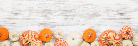 Autumn farmhouse pumpkin bottom border over a white wood banner background. Rustic orange and white cloth pumpkins. Top view with copy space.の写真素材