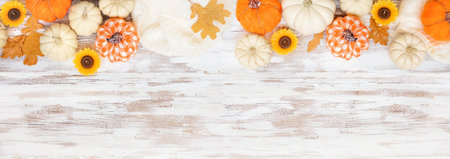 Autumn country farmhouse top border over a white wood banner background. Orange and white cloth pumpkins, sweater, candles and fall leaves. Above view with copy space.の写真素材
