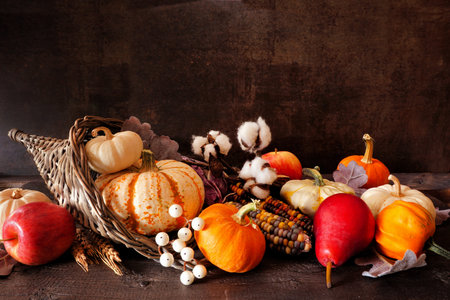 Thanksgiving harvest cornucopia filled with autumn fruits and vegetables. Side view against a dark...
