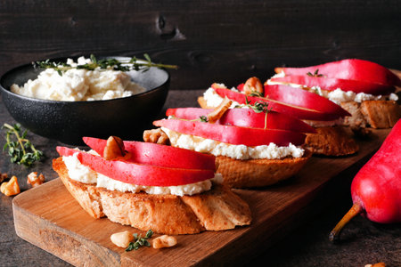 Crostini appetizers with red pears, whipped feta cheese and walnuts. Close up table scene against a dark wood background. Party food concept.の写真素材