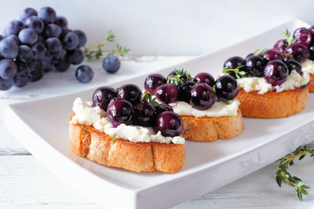 Crostini appetizers with roasted grapes and whipped feta cheese. Close up table scene against a white background. Party food concept.の写真素材