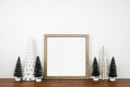 Christmas mock up with wooden frame and tree decor. Square frame on a wood shelf against a white wall. Copy space.の写真素材