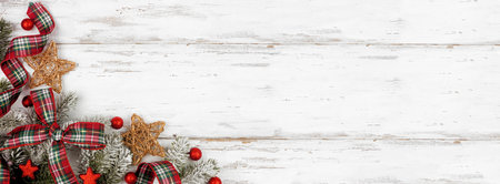 Christmas corner border of ornaments, branches and red and green plaid bows and ribbon. Top down view on a white wood background. Copy space.の写真素材