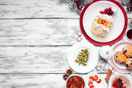 Christmas breakfast side border. Overhead view on a white wood background. Fun holiday food concept. Santa pancakes, scones, fruit and cereals. Copy space.の写真素材