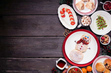 Christmas breakfast side border. Top view on a rustic dark wood background. Fun holiday food concept. Snowman pancakes, scones, fruit and cereal. Copy space.の写真素材