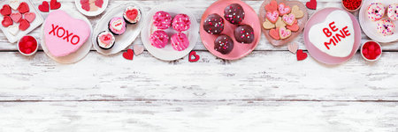 Valentines Day top border with assortment of fun desserts and sweets. Overhead view on a white wood...