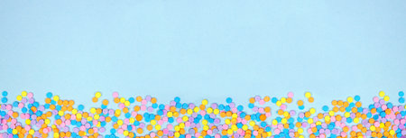 Colorful candy sprinkles bottom border. Top down view on a blue banner background. Pastel Easter color theme. Copy space.の写真素材