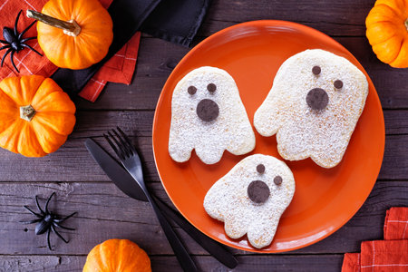 Cute Halloween ghost pancakes. Top view on an orange plate against a dark wood table background.の写真素材