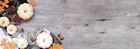 Cozy autumn corner border with blanket, white pumpkins, leaves and natural decor. Above view over a grey wood banner background. Black, white and brown theme.の写真素材