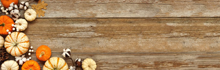 Fall corner border of pumpkins, leaves and natural decor over a rustic wood banner background. Top down view with copy space. White, brown and orange colors.の写真素材