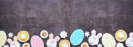 Easter or spring themed baking bottom border with assorted cookies and sweet desserts. Top down view on a dark stone banner background with copy space.の写真素材