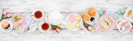 Easter or spring tea table scene against a white wood banner background. Assortment of finger sandwiches, scones and sweet desserts. Above view.の写真素材